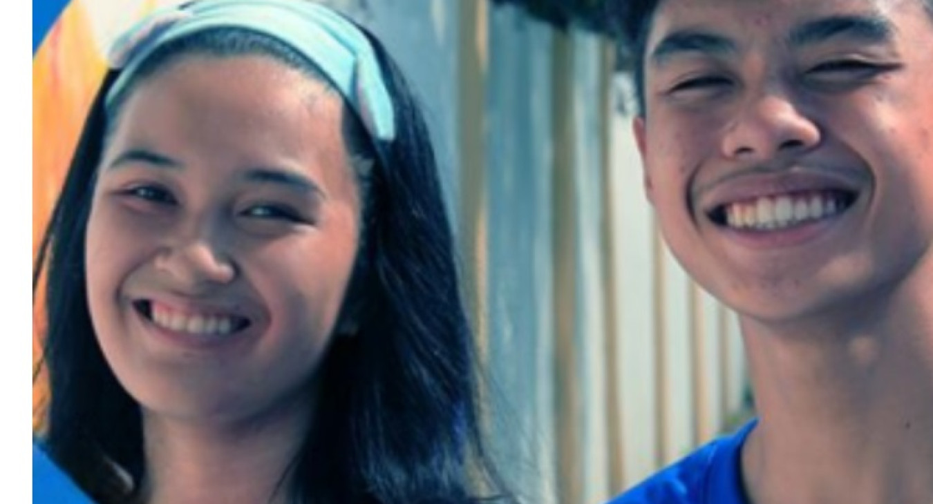 The photo features an adolescent girl and an adolescent boy smiling and wearing blue shirts