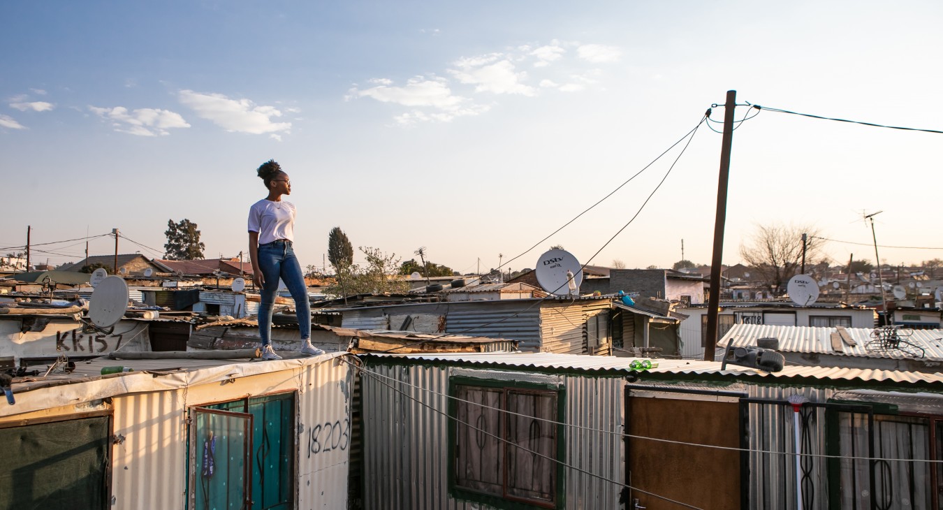 Adolescent girl standing on roof of house in informal settlement