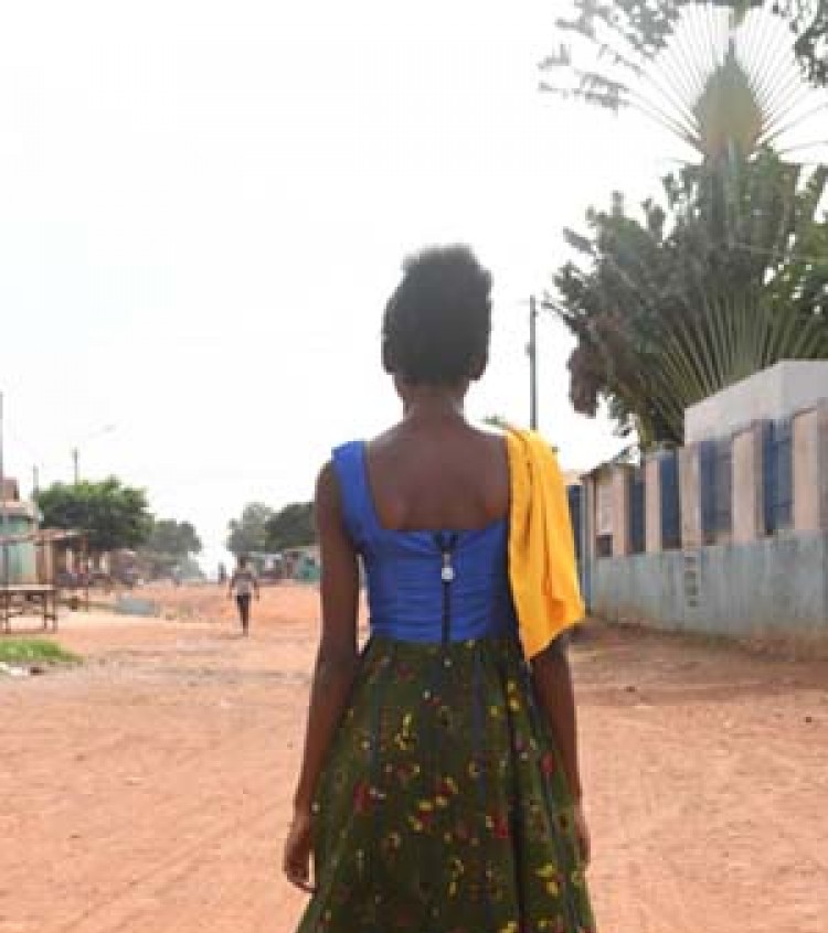A young woman stands on a dusty street with her back to camera
