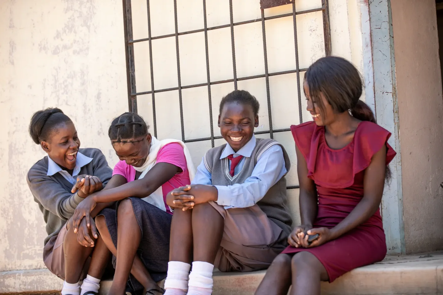 Four adolescent girls sit together outside a building, laughing and sharing a moment of joy.